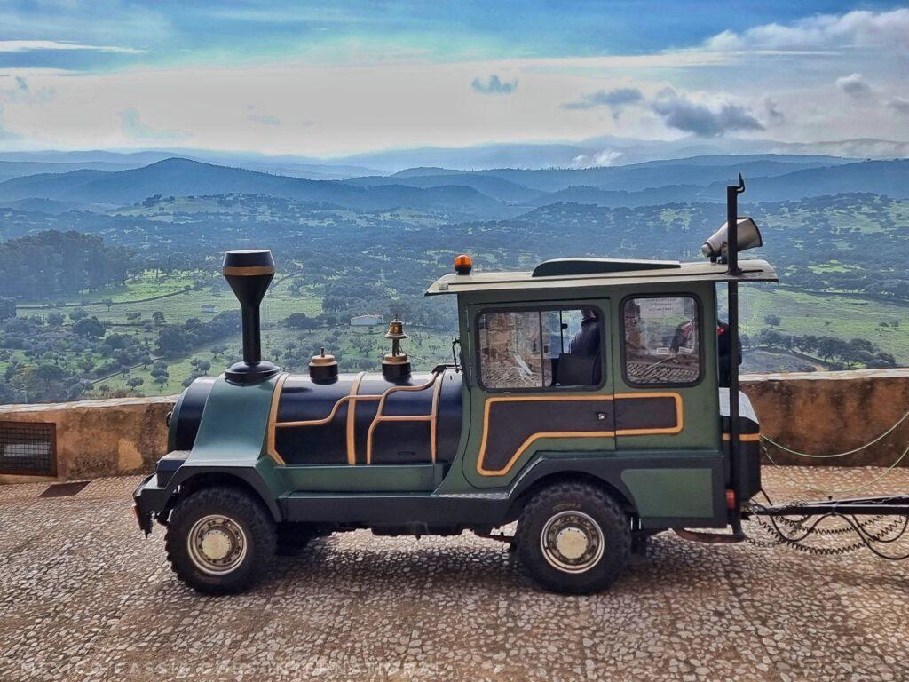 small green tourist train car in front of gorgeous view over fields and hills