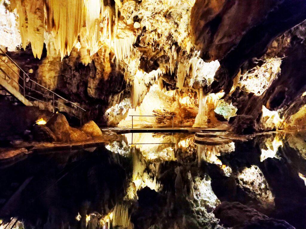 photo of inside of cave with stalactites over dark water 