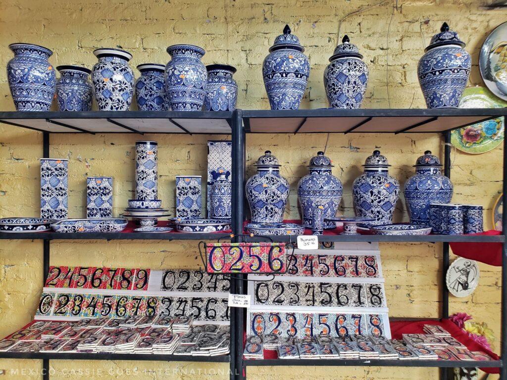 shelves of blue and white ceramic jars with lids. ceramic house numbers on shelf below