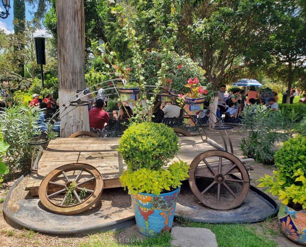 park scene - artistic rendition of a flattened cart. potted plant in front, trees and people behind