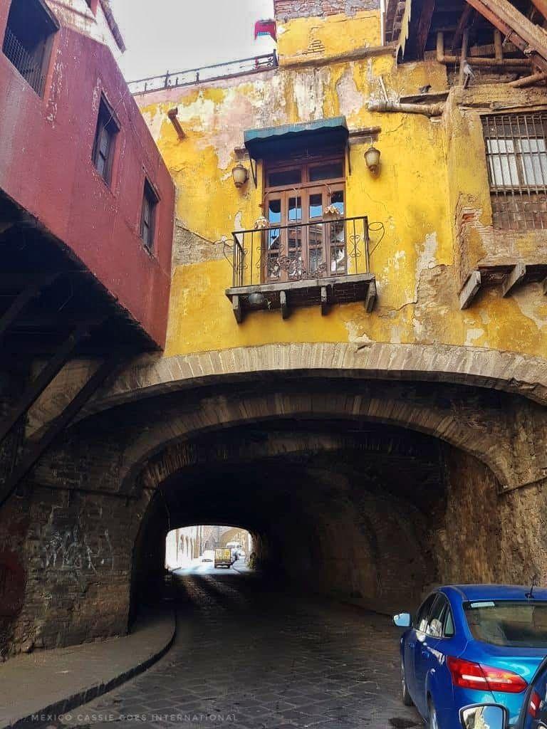 car tunnel / arch under a yellow house. blue car on right of photo