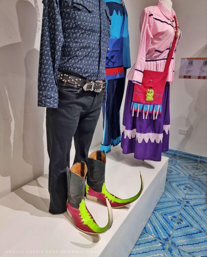 traditional Mexican outfits: black trousers, shirt, belt and wild curled up at the end leather shoes (yellow & red). Women's outfit behind - purple skirt, red bag, pink shirt