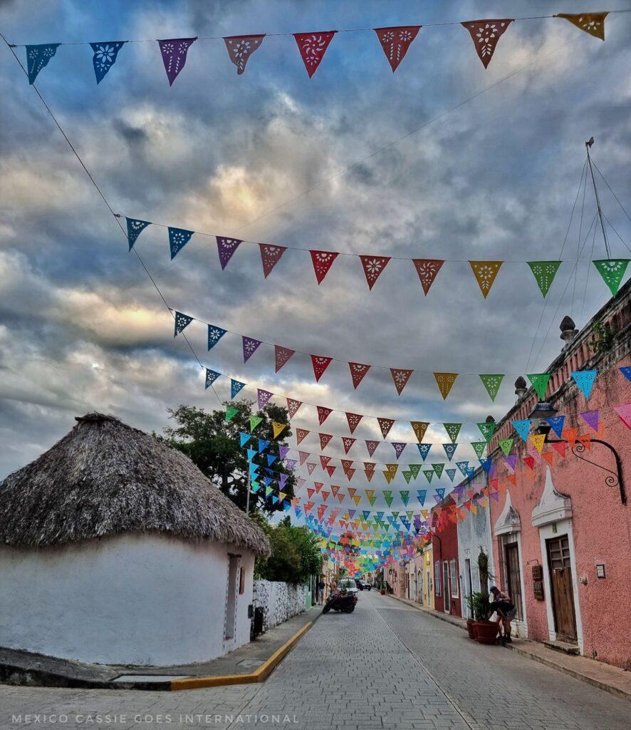 street shot, white thatch building on left, pink building on right, bunting stretched over street