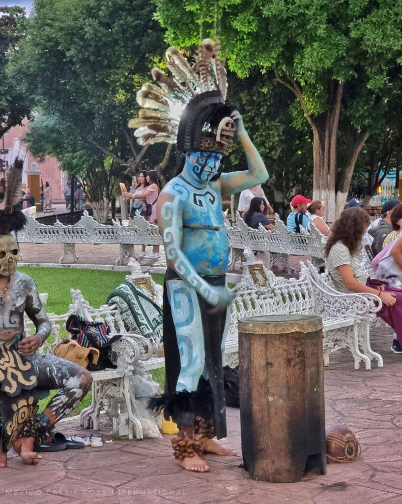 man in traditional Maya blue body paint beating a drum