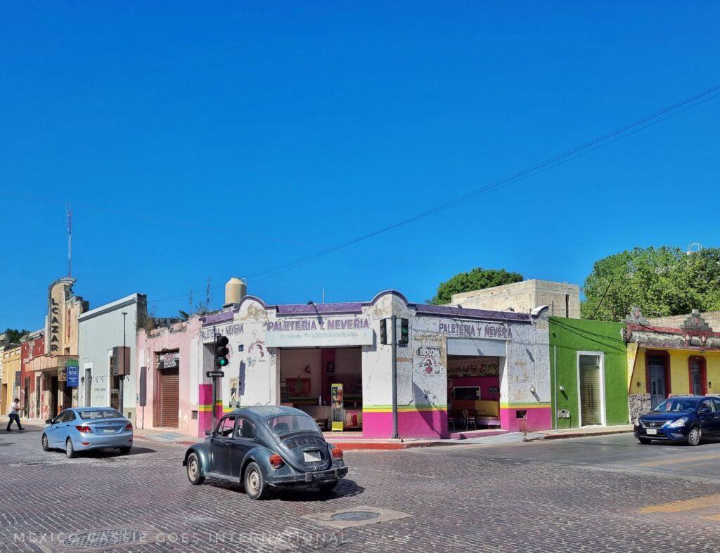 road scene - 1 storey white and pink building, 3 cars on road. blue sky