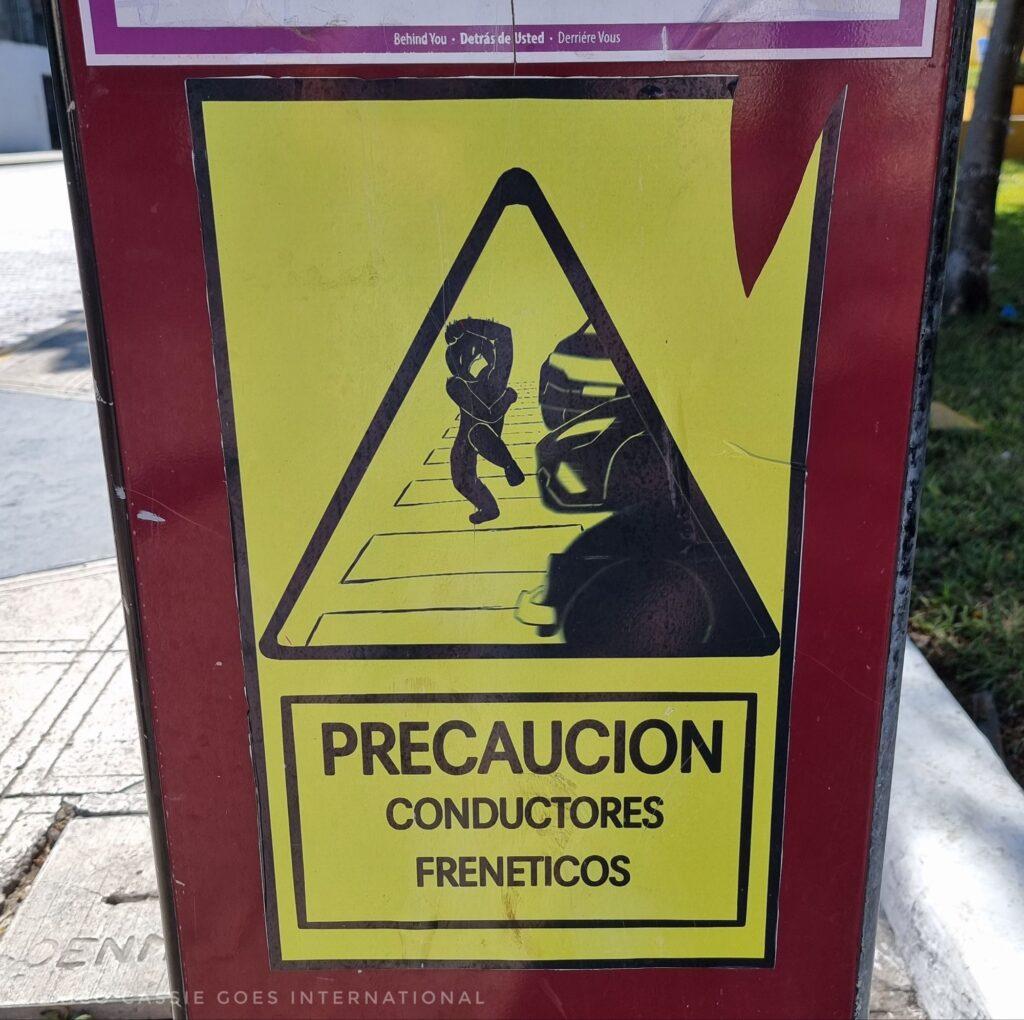 yellow sign that says "precaucíon conductores freneticos" (warning: frenetic drivers). triangle with a pic of a person on a pedestrian crossing cowering by cars