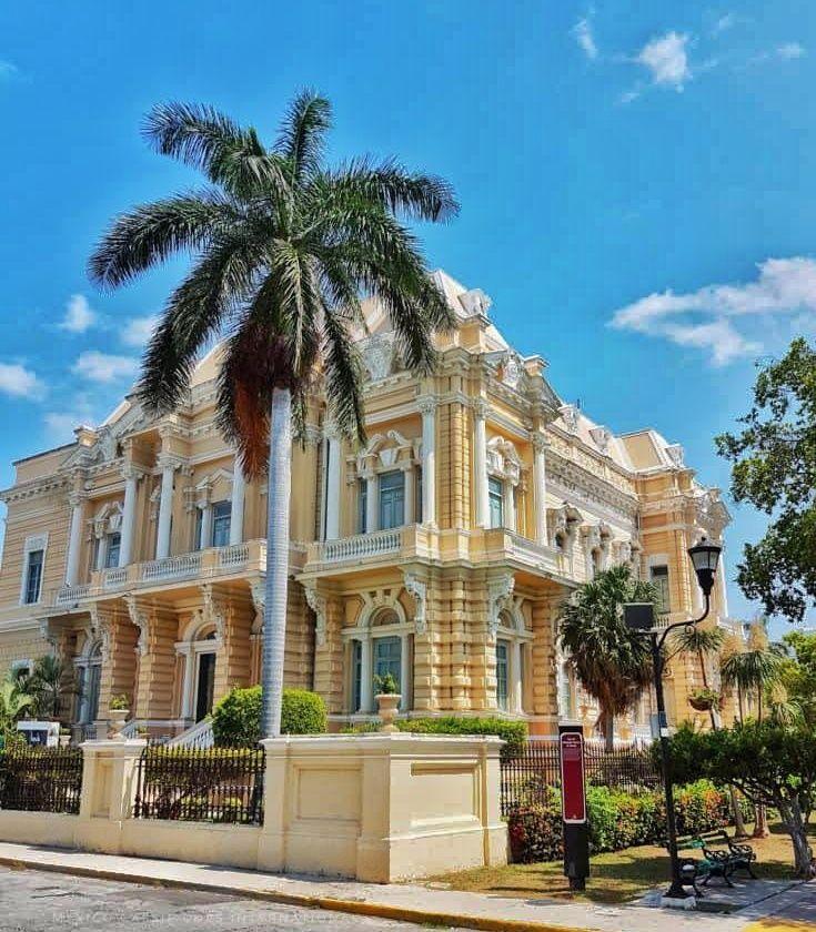 large peach coloured mansion, palm tree in front and blue sky above