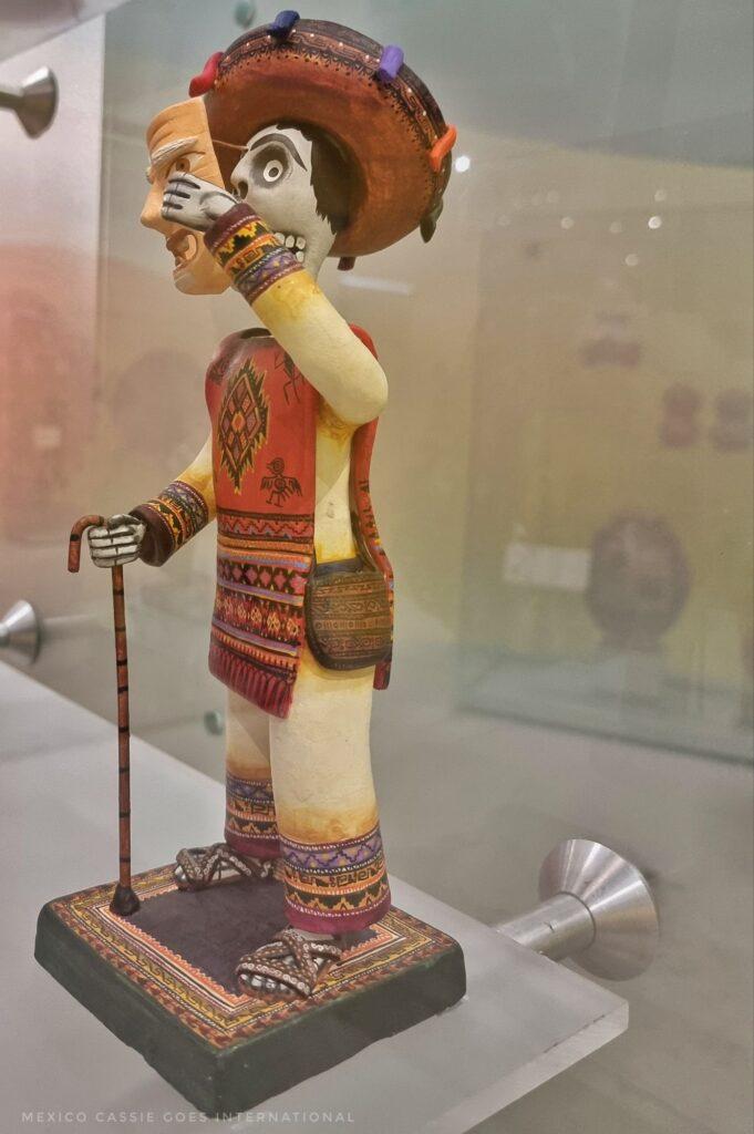 small figurine of a man taking off his mask to reveal the skull underneath