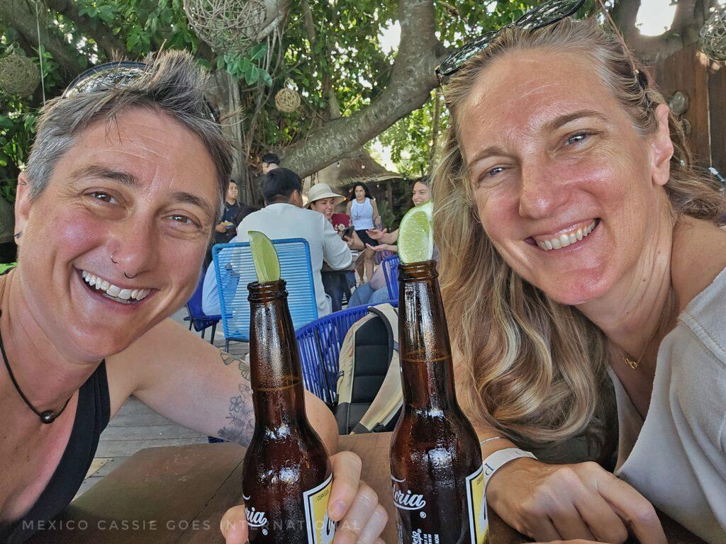 2 smiling people in an outside restaurant. 2 bottles of beer with lime sticking out top on table