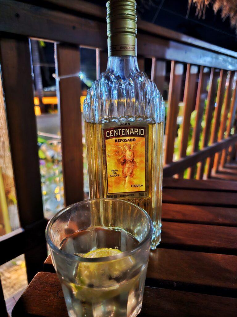 bottle of Centenario tequila and one glass on a wooden table