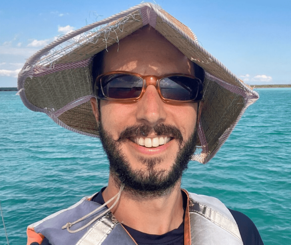 photo of man in straw hat and sunglasses. he has a beard, is wearing a straw hat and a lifejacket