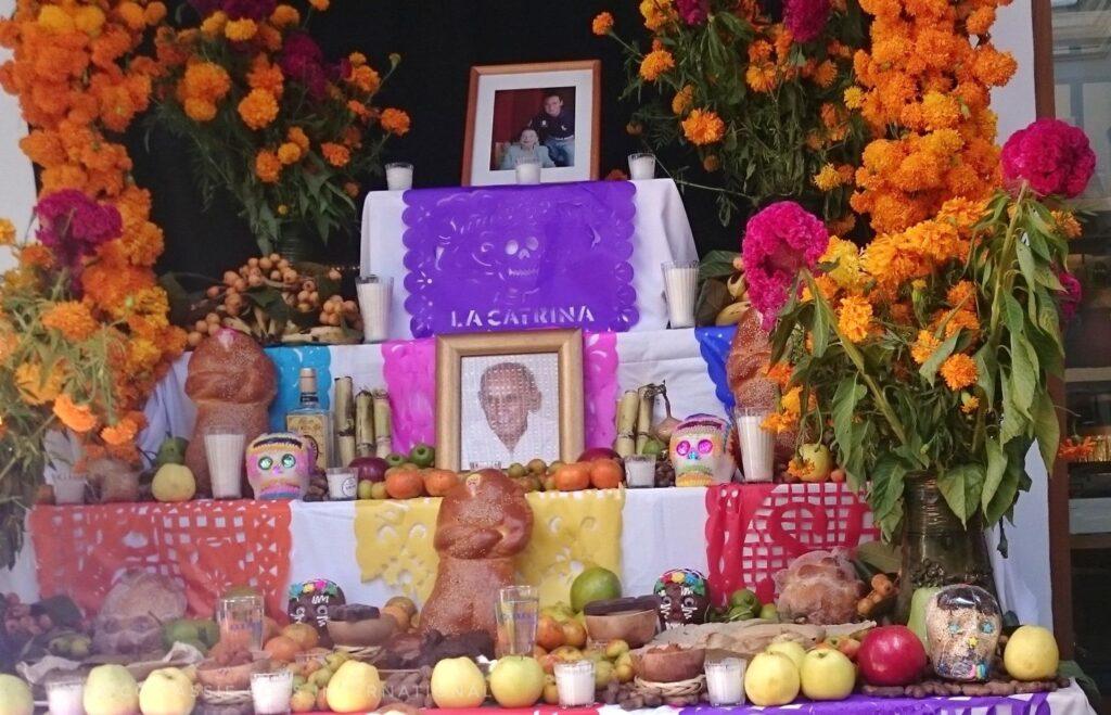 typical day of the dead altar with photos, papel picado, flowers, food and candles