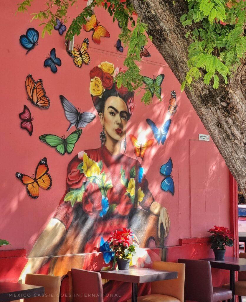 street art painting of Frida Kahlo with butterflies around her - tables and chairs in front of painting