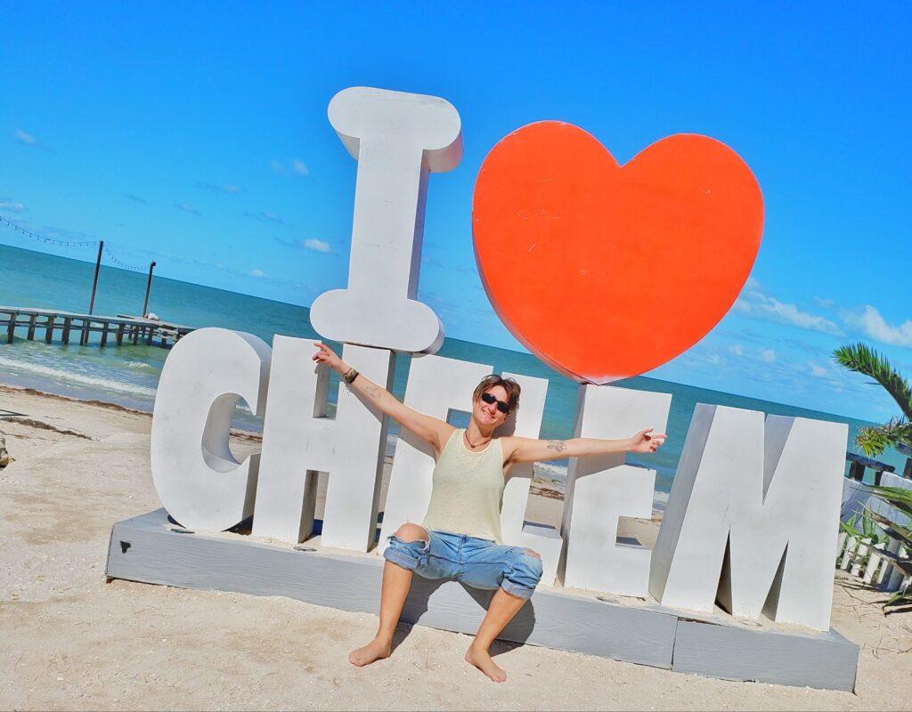 Cassie sitting in front of an I heart Chelem sign (red heart), sea behind