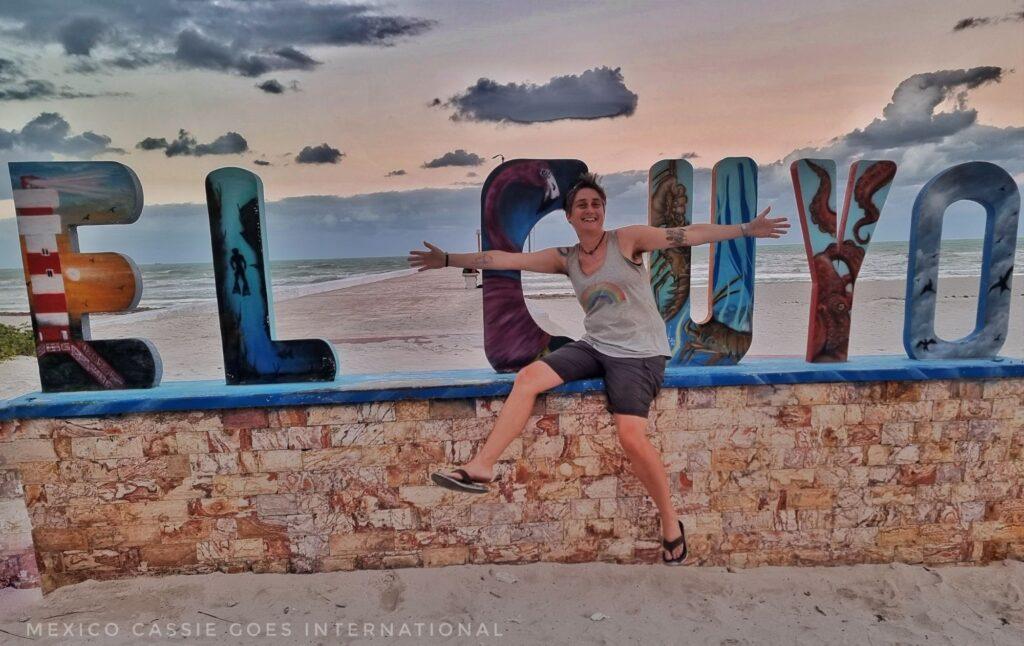 MexicoCassie, arms outstretched in front of the El Cuyo letters at dusk