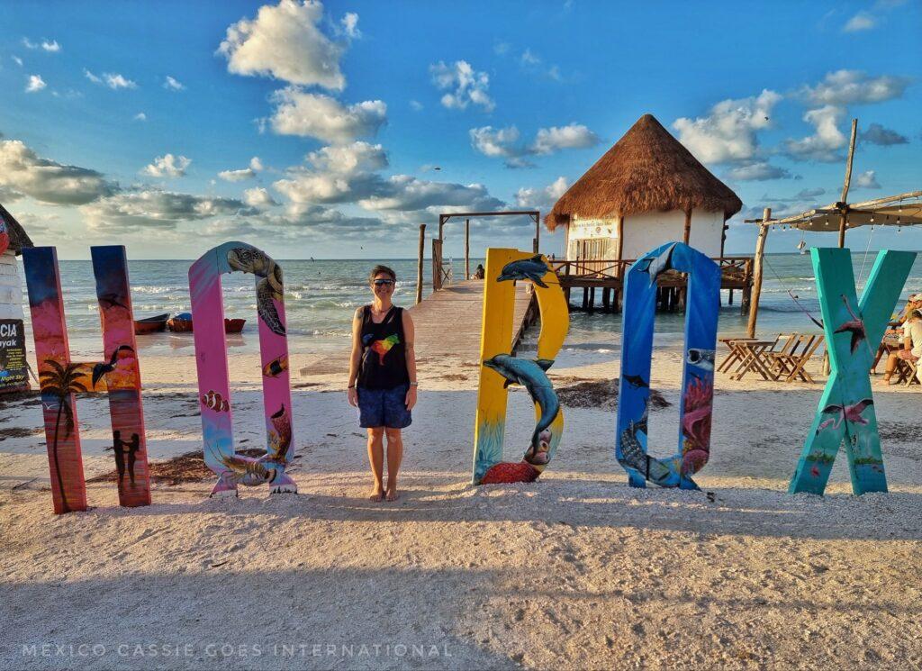 Holbox letters where Cassie is the L (dressed in black tshirt and blue shorts). Early dusk over sea behind