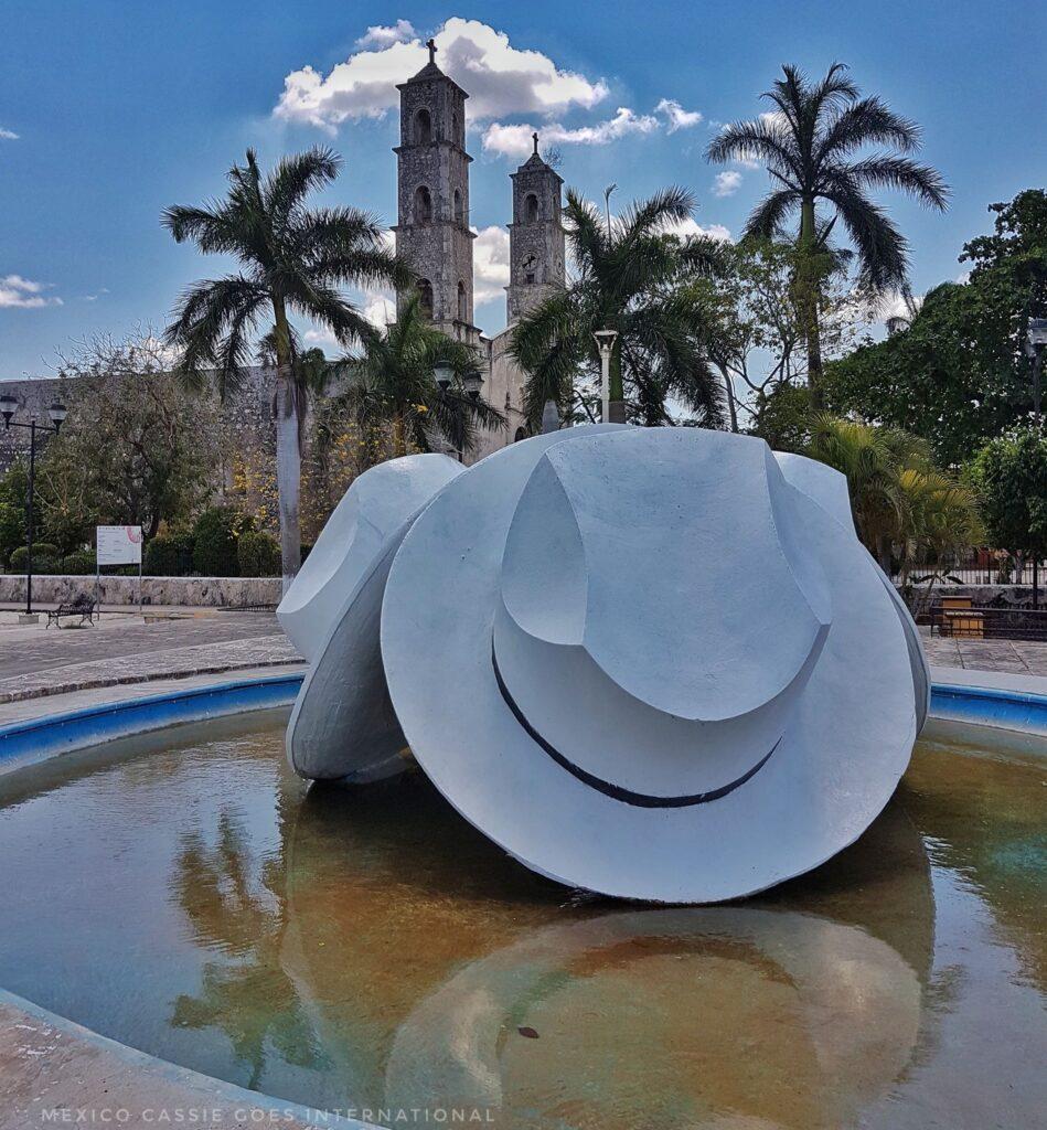 panama hat sculpture surrounded by water (nice reflection), church and palm trees behind
