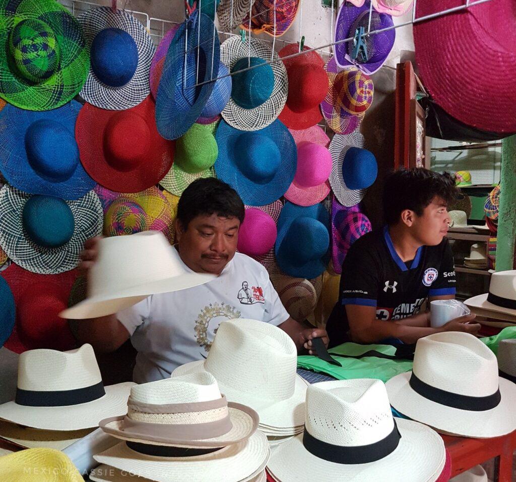 man and boy in hat shop - white hats with black bands on table in front of them, colourful hats on wall behind them