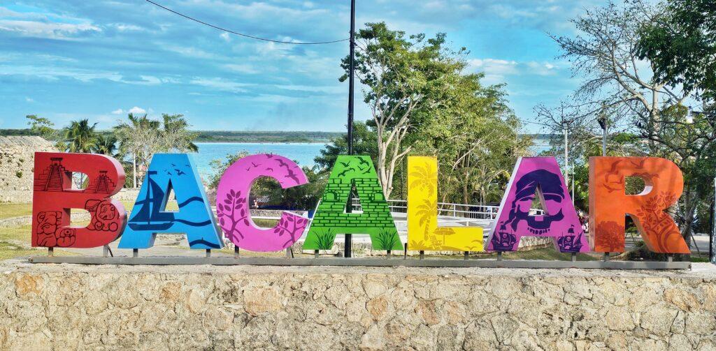 Brightly coloured Bacalar letters against blue sky (trees behind and you can just make out the blue water)