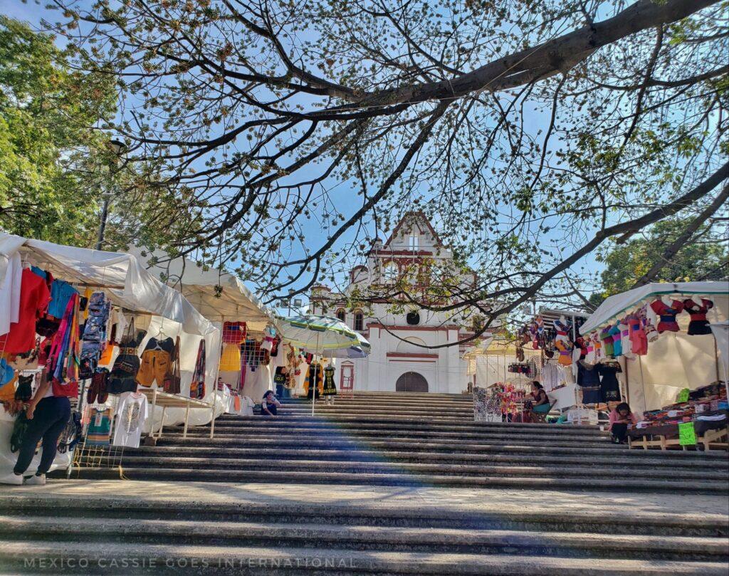 photo taken looking up steps to a large white church- branch over front of photo and stalls on sides