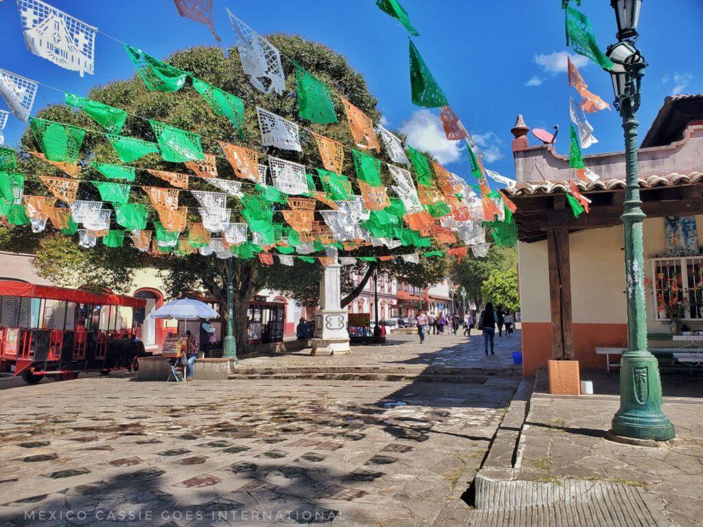sunny plaza scene, green, red & white bunting flying, shadows on ground