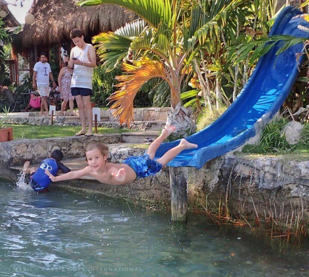 kid in blue shorts flying off end of blue slide over water - looking at camera