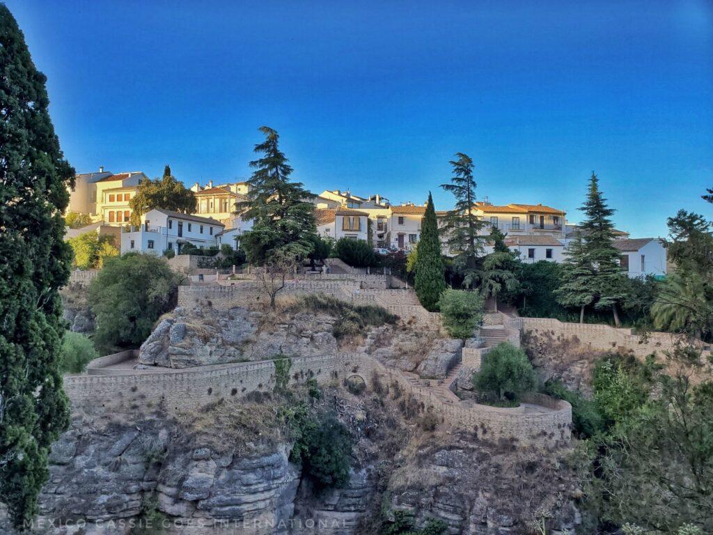 concrete pathway built onto top of rock face. trees and white houses