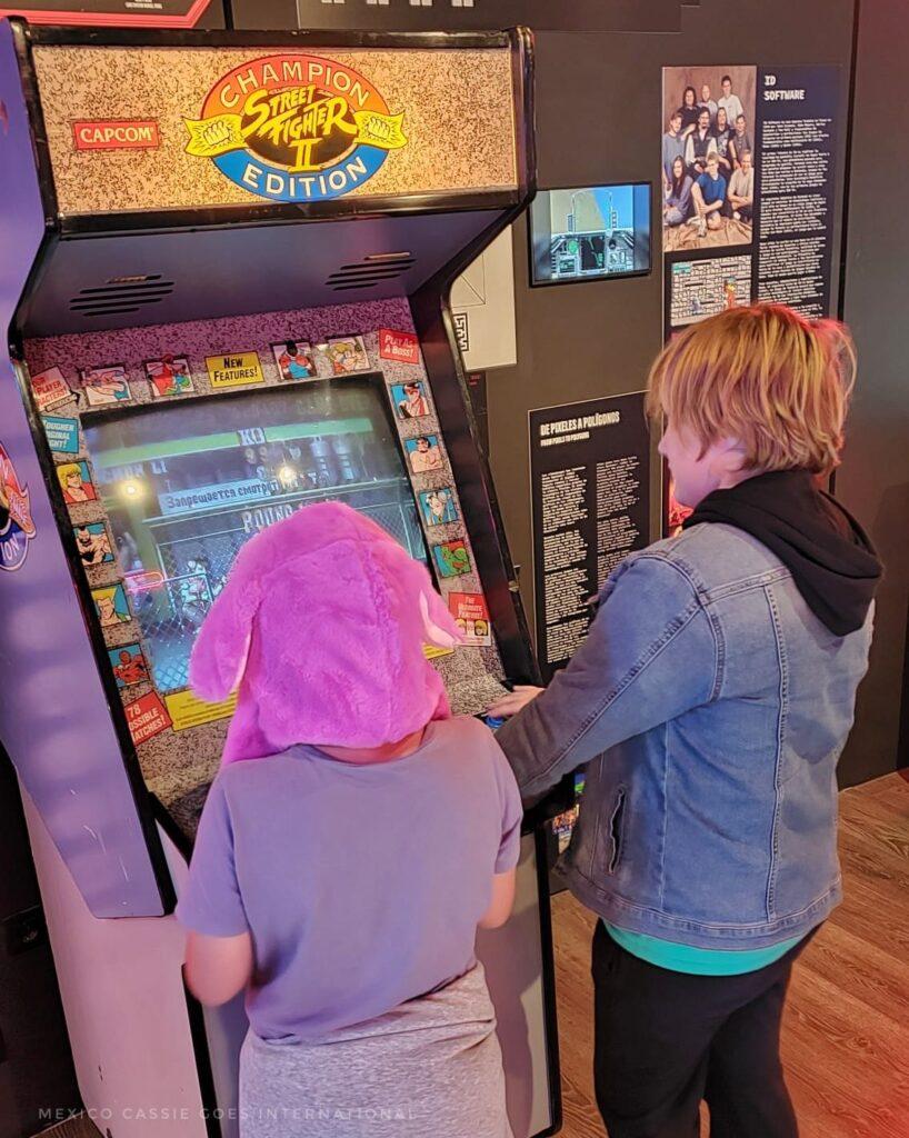 2 kids standing at a street fighter II game machine