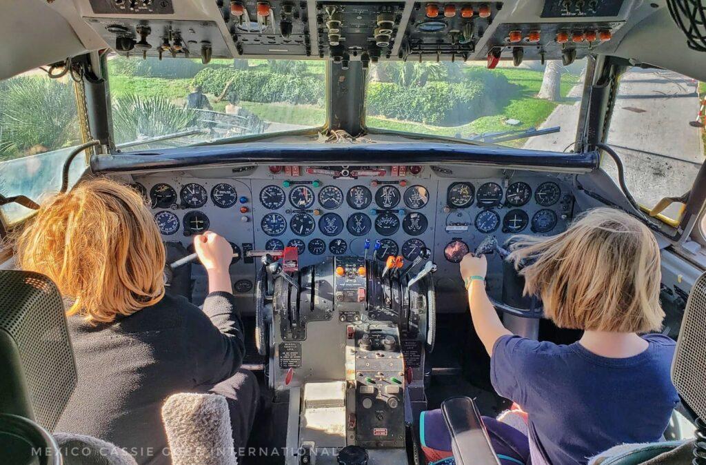 2 kids sitting in cockpit of old plane