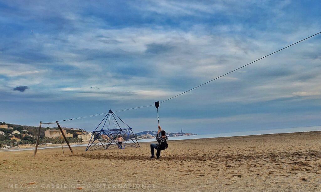 kids and a dad playing on beach playground - man on zipline, kids on netted pyramid