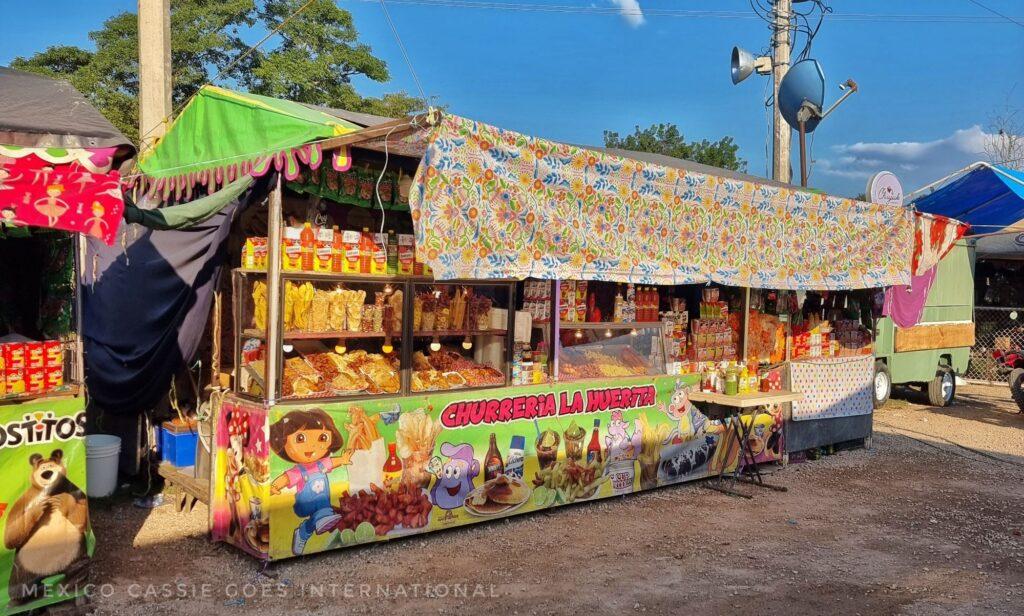 long stall selling fried foods. the main covering at the base has drawings of kids cartoon characters on it - says churreria la huerta