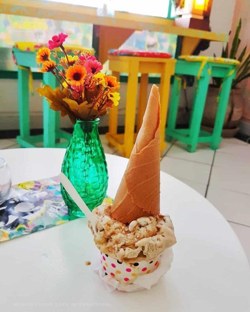 upside down ice cream cone and ice cream, green vase with flowers in it on table. green stools in background