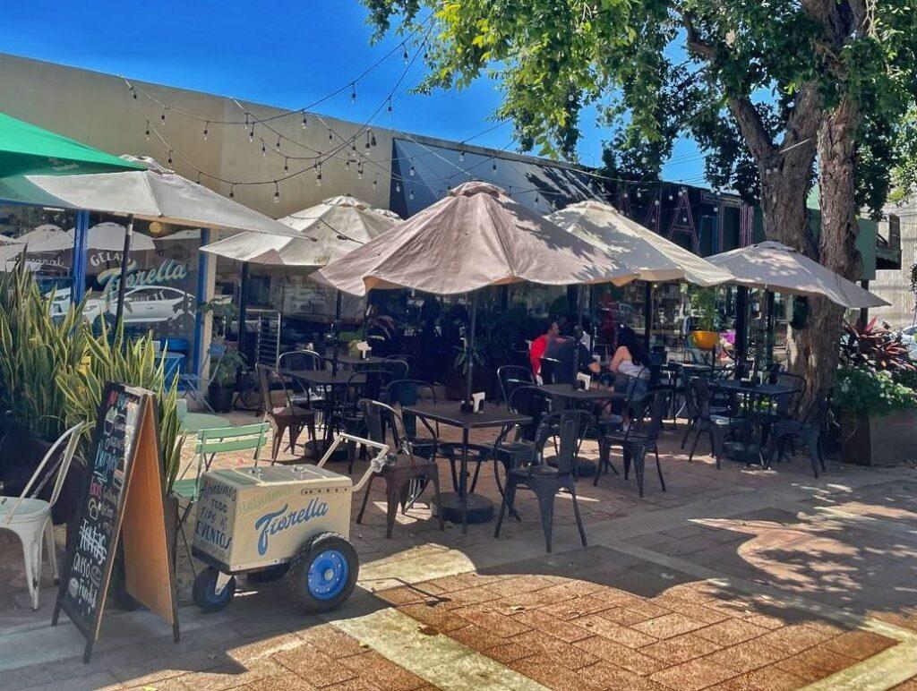 view of outdoor space of ice cream store - umbrellas over tables, ice cream cart in left of picture