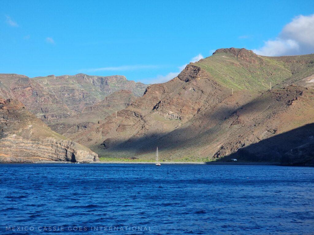 sea, boat entering cove, green covered low mountains, sky