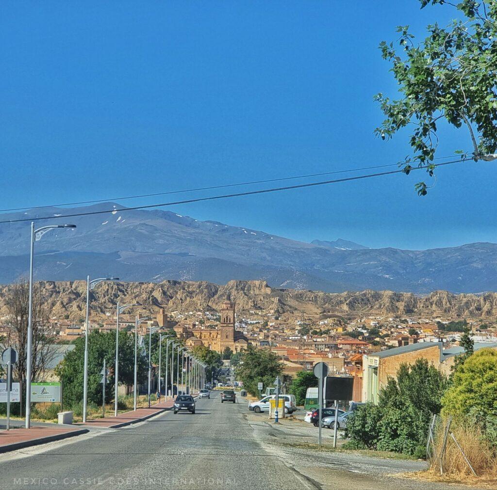 empty road stretching into Guadix town, mountains in background