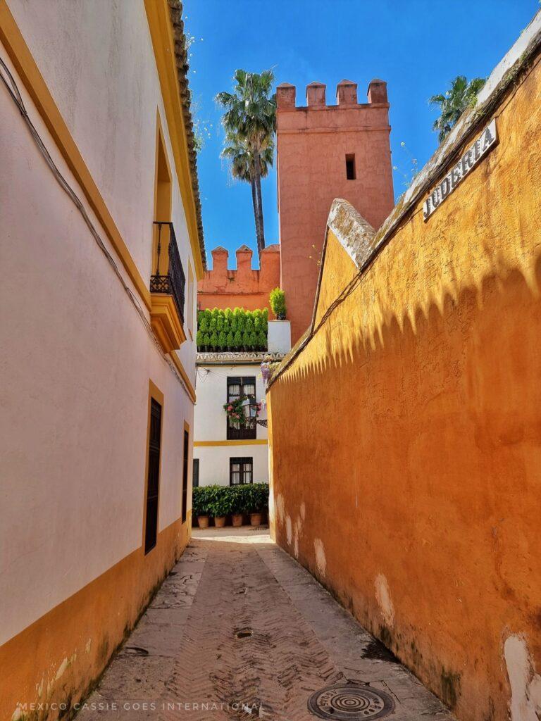 narrow street, yellow wall on right, white wall on left, castle turret ahead