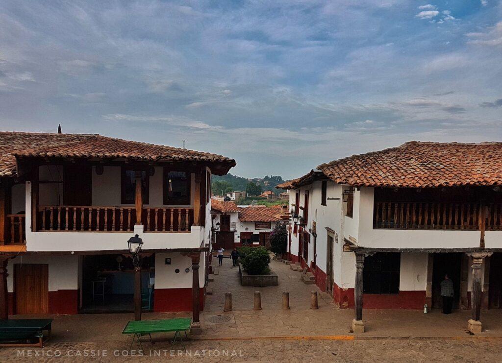 looking down over white and red painted houses and a plaza. Buildings have wooden balconies.