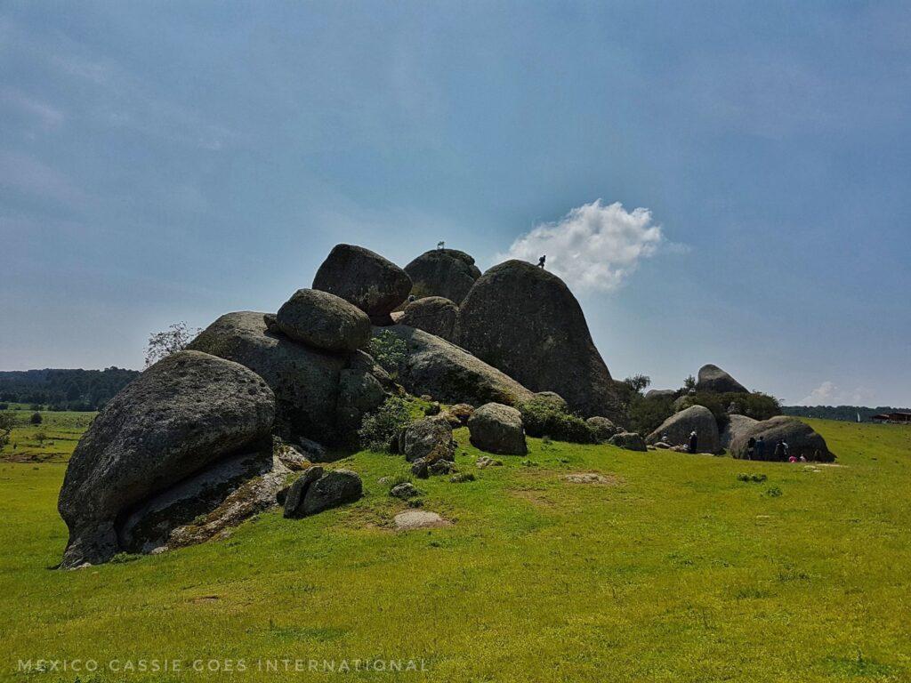blue sky, green grass, monolithic rocks in middle of photo. people walking on them (small figures because rocks are so big)