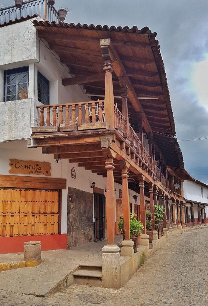 2 storey white building with wooden balcony supported by columns