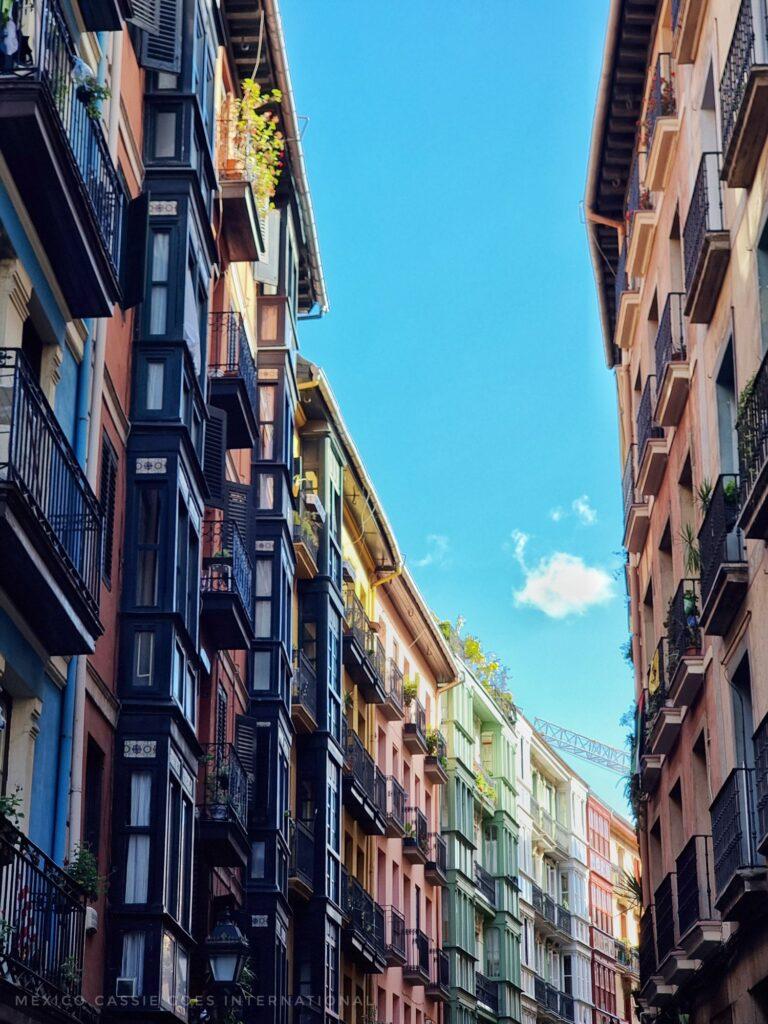 Bilbao's casco antiguo (old city) - photo contains beautiful tall buildings on either side of a curved road, all different colours with wooden window boxes and blue sky
