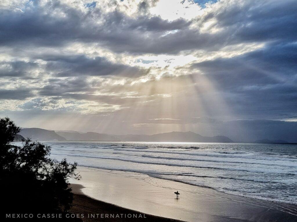 solitary surfer on the beach on a cloudy evening, sun's rays coming through cloud