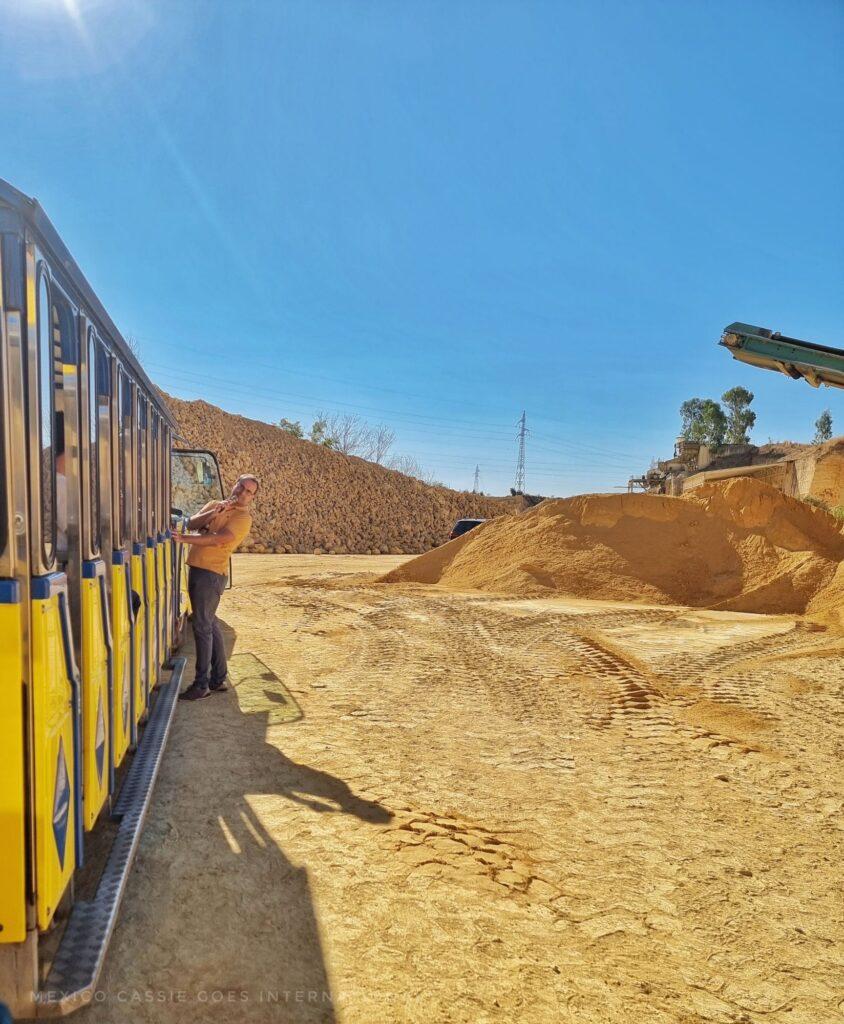 photo taken looking along the side of a yellow tourist train in a quarry of yellow sands. Man in yellow tshirt standing at far end of train