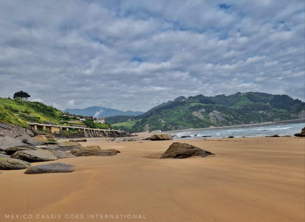 beach - sand with a few rocks, hills in background