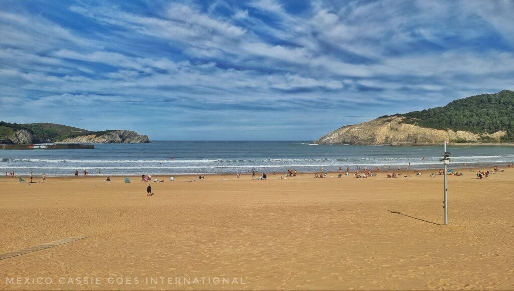 wide expanse of sandy beach, blue sea in a wide bay, a few people on the beach in the distance