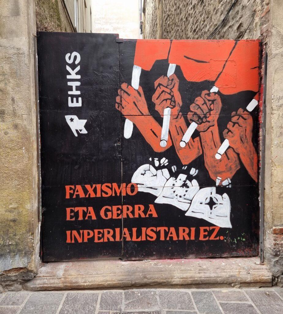 4 hands holding red flags crushing helmets. reads, "faxismo, eta gerra inperialistariez"