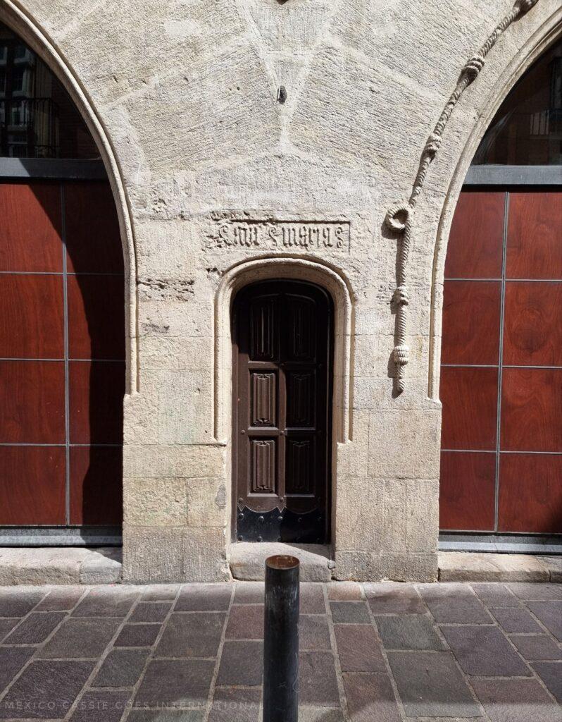 tiny door in medieval wall between two bigger doors, both only half in photo