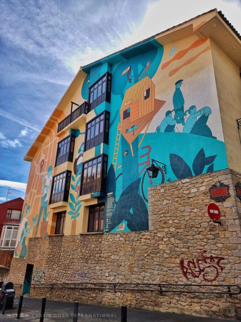 wall painted with pro educational pictures, people sitting, tree house, blues and yellows
