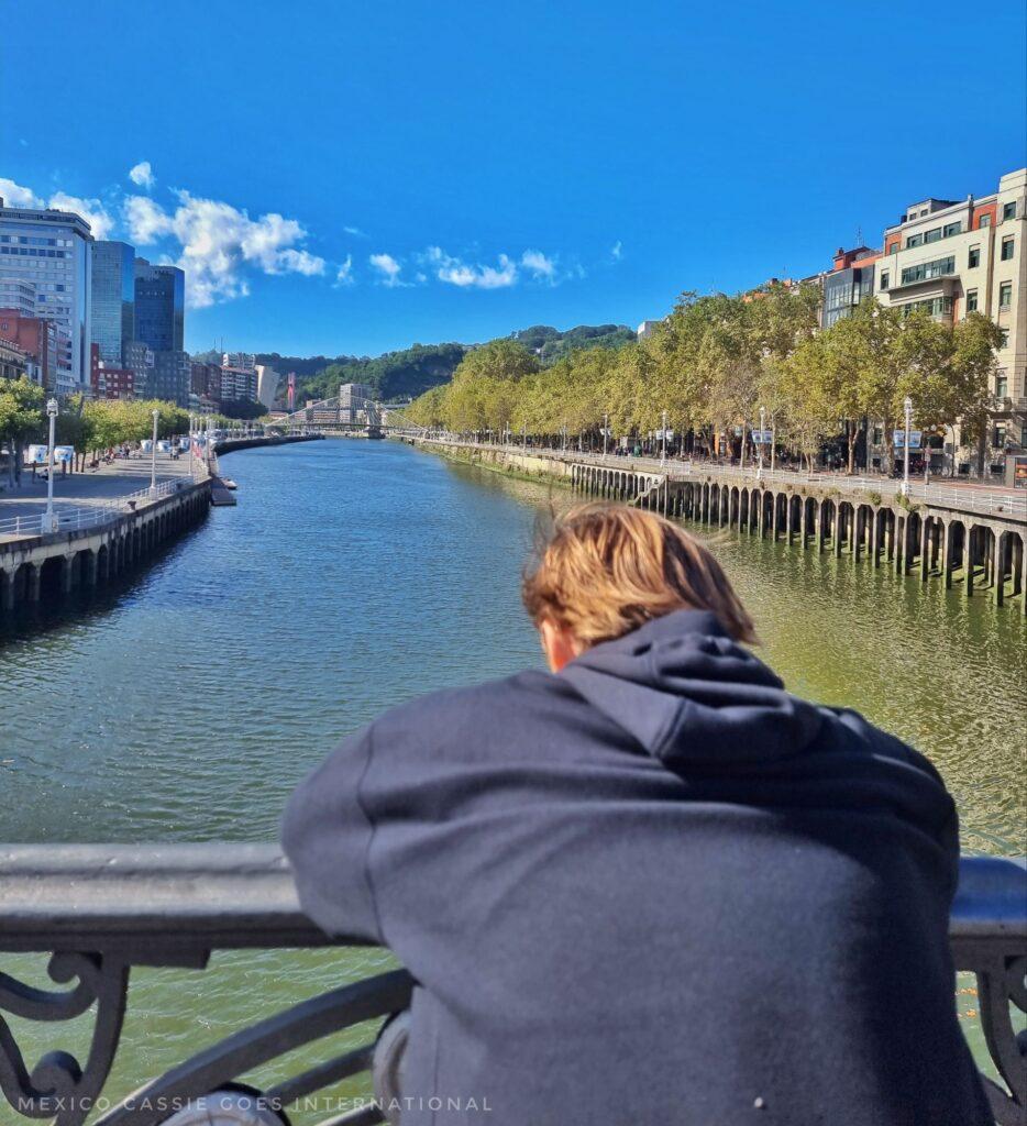 kid in black hoodie watching fish in river from a bridge