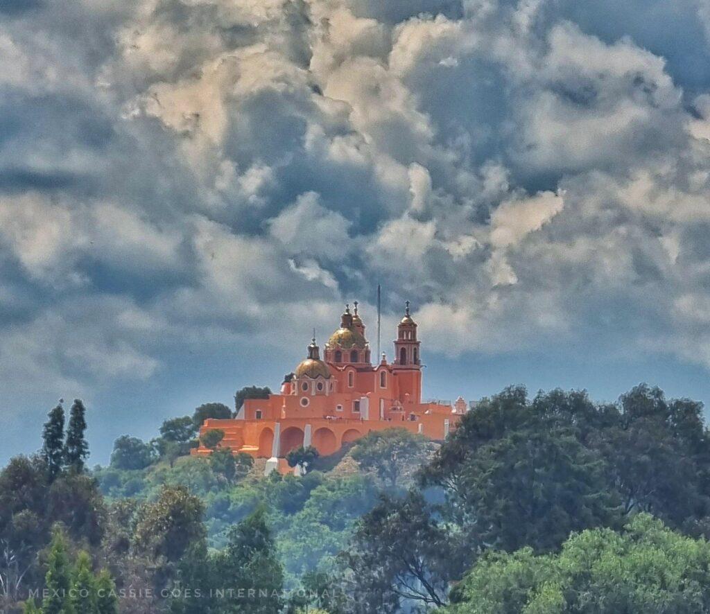 view of yellow church on hill - clouds behind and trees in front