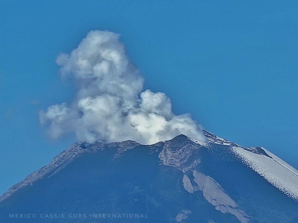 close up of top of smoking volcano, blue sky and some snow on one side